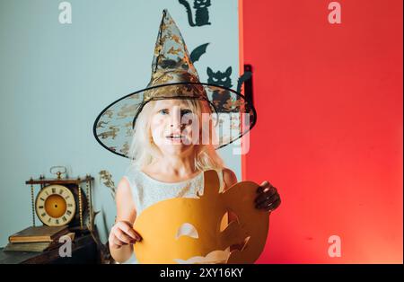 Halloween ragazza cute felice con le zucche su uno sfondo halloween. Festa di Halloween. Concetto di vacanza per bambini. Decorazione domestica di Halloween. Foto Stock