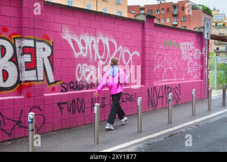 Milano, Italia - 23 giugno 2024: Ragazza in una giacca a vento rosa che cammina lungo un muro rosa ricoperto di graffiti nella zona di Tortona Foto Stock