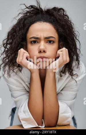 Una giovane donna afroamericana poggia il mento sulle mani, persa nella contemplazione. Foto Stock