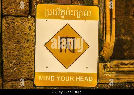 Cartello bilingue "Mind Your Head". Tempio di Banteay Srei, parco archeologico di Angkor, provincia di Siem Reap, Cambogia. © Brooks Lieb Foto Stock