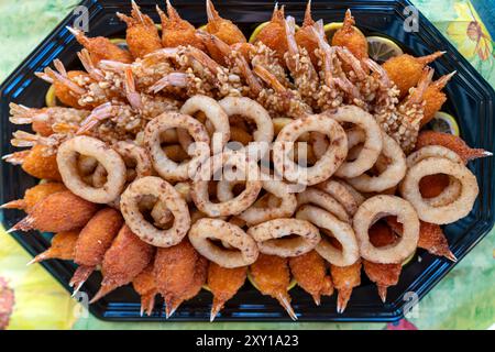 Un vivace assortimento di gamberi fritti e anelli di cipolla esposti splendidamente su un vassoio nero Foto Stock