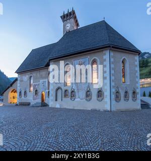 Paesaggio urbano con vista laterale della chiesa dei santi Filippo e Giacomo, girato al crepuscolo con la luce brillante dell'estate a Campitello di Fassa, Italia Foto Stock