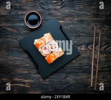 set di sushi roll con soia e bacchette su sfondo nero in legno Foto Stock