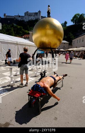 Ein Mann sonnt sich vor der Skulptur Sphaera von Stephan Balkenhol am Kapitelplatz, Salisburgo 6.08.2024 *** Un uomo che prende il sole di fronte alla scultura Sphaera di Stephan Balkenhol su Kapitelplatz, Salisburgo 6 08 2024 Foto Stock