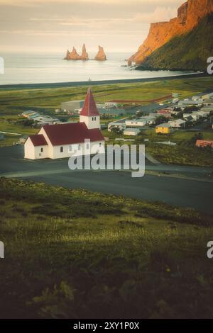 La chiesa nella città costiera di Vik, nel sud dell'Islanda, con l'oceano e le montagne marine in lontananza, Reynisdrangar e l'oceano Atlantico, famou Foto Stock