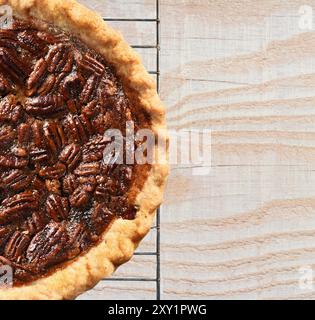 Vista ad angolo alto di una torta di pecan appena sfornata su una griglia rinfrescante in cima ad un tavolo da cucina in legno rustico. Solo metà della torta viene visualizzata lasciando spazio per la copia. Foto Stock