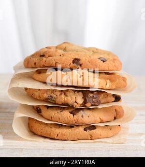 Primo piano di una pila di biscotti appena sfornati Chocolate Chip, uvetta d'avena, biscotti White Chocolate Chip su carta pergamena. Formato quadrato su un rustico W Foto Stock