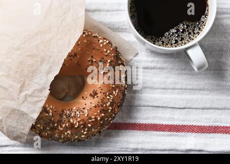 Bagel fresco e tazza di caffè caldo su un asciugamano da tè. Vista ad angolo elevato in formato orizzontale. Foto Stock