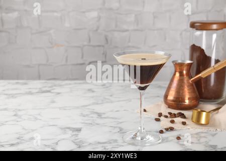 Cocktail rinfrescante in vetro, fagioli, caffè macinato e cezve su tavolo in marmo bianco, spazio per testo Foto Stock