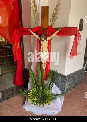 Una statua di Cristo sulla croce all'ingresso della Chiesa di nostra Signora del Rosario, Monteros, Argentina. Decorato con foglie di palma per Palm Sun Foto Stock