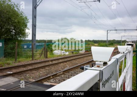 Irlam, Manchester, Regno Unito, agosto 26, 2024: attraversamento di binari rurali con un cielo nuvoloso sullo sfondo e fogliame verde. Foto Stock