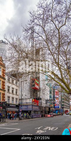 Strada nel centro di Londra con un edificio in costruzione con ascensore in metallo rosso o ascensore con griglie protettive per un ponteggio e un truc Foto Stock