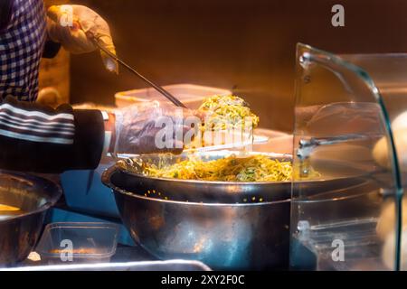 Chef cinese che indossa grembiule e guanti di plastica che cucinano con ingredienti in una ciotola per preparare gnocchi in cucina di una stal da asporto cinese e asiatico Foto Stock