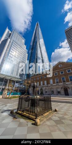 Vista ad angolo basso da un cortile del moderno grattacielo di vetro The Shard con cielo blu e nuvole riflesse nelle sue finestre e due amici seduti Foto Stock