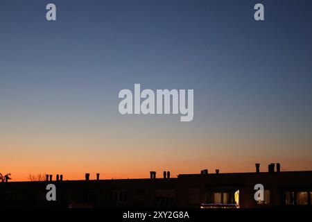 Cielo crepuscolo vivace sui tetti urbani con camini sagomati su sfumature di arancione tenue e blu intenso del tramonto. Accattivante scena serale. Foto Stock