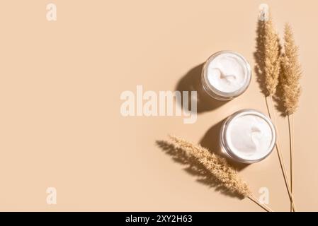 Panna di collagene in vasetti aperti e erba secca di canne su sfondo beige, vista dall'alto, spazio di copia. Prodotti di bellezza naturali anti-età per la cura della pelle e del corpo des Foto Stock