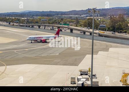 San Francisco, California, Stati Uniti - 2 agosto 2024. Aeroplano rullante sulla pista di un aeroporto con traffico autostradale sullo sfondo. Foto Stock