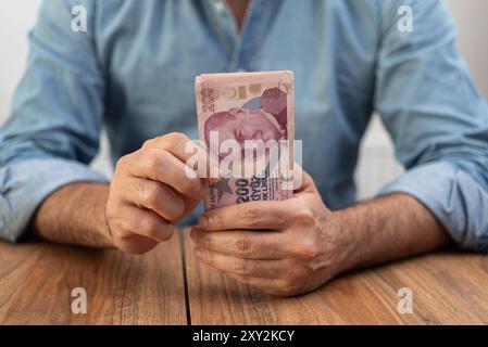 Uomo che regge una pila di banconote della lira turca su un tavolo di legno. Concetto economico che illustra l'inflazione e la finanza in Turchia Foto Stock