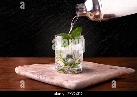 Il Mojito viene versato in un bicchiere di whisky su un tagliere Foto Stock