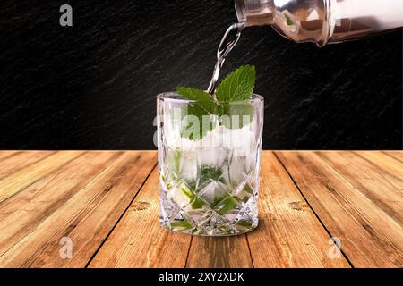 Il Mojito viene versato in un bicchiere di whisky su un tavolo di legno Foto Stock