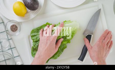 Donna che prepara insalata di sedano con lattuga romagina. Primo piano di foglie di lattuga verde fresca su un tagliere bianco, piatto Foto Stock