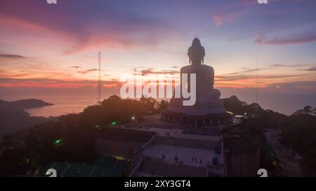 Una suggestiva sagoma della statua del grande Buddha adagiata contro un vibrante cielo crepuscolo all'orizzonte. La statua si affaccia su un tranquillo paesaggio costiero, cre Foto Stock