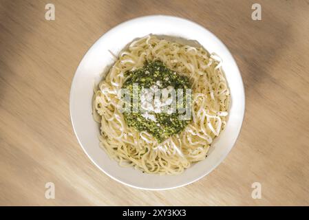 Tagliatelle fresche condite con pesto al basilico in una ciotola su una superficie di legno, vista dall'alto Foto Stock