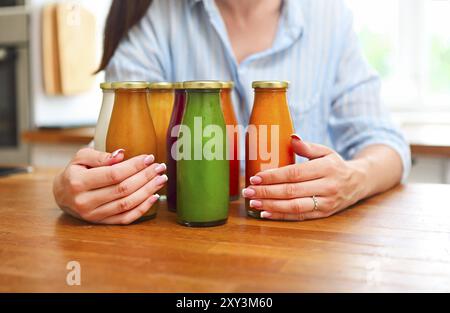 Nutrizione dietetica con succo disintossicante. Donna sana che posa con bottiglie di succo fresco di frullato disintossicante. Primo piano di una bella ragazza in forma felice in cucina Foto Stock