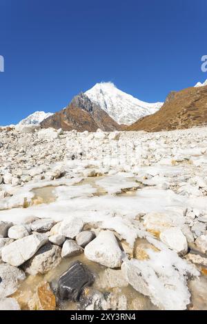 Gelido fiume alpino in esecuzione attraverso white terreno roccioso paesaggio ad alta quota tundra alpina con Langtang Lirung sfondo picco vicino Kyanjin Gompa Foto Stock