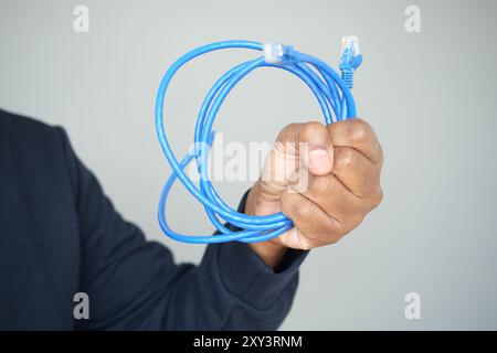 Un primo piano di mani che reggono un cavo Ethernet blu a spirale per una connessione di rete Foto Stock