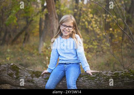 Ritratto di una ragazza bionda con gli occhiali all'aperto nel parco in autunno sfondo parco seduti sulla struttura ad albero Foto Stock