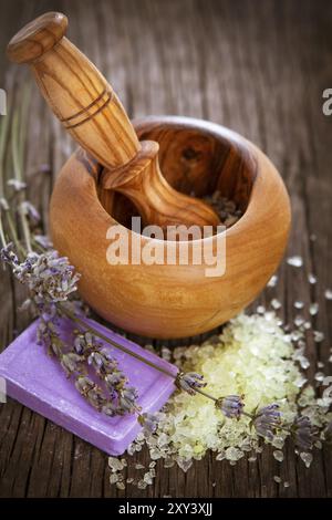 Da sopra composizione con sapone naturale fatto a mano con lavanda e sale marino posto accanto a Malta di legno con pestello su sfondo di legno Foto Stock