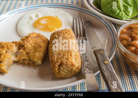 Primo piano di deliziose crocchette fatte in casa e uova fritte su un piatto bianco con verdure fresche e fagioli bianchi in salsa di pomodoro Foto Stock