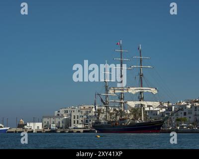 Grande nave a vela nel porto di fronte a una città costiera bianca, acque calme e cielo azzurro limpido sullo sfondo, ibiza, Mar mediterraneo, Foto Stock