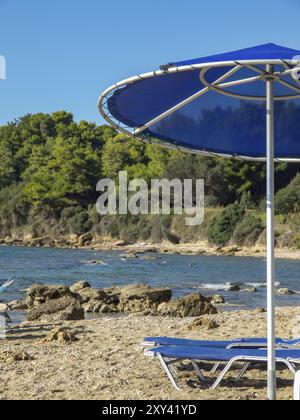 Ombrellone blu e sdraio sulla spiaggia con vista sul mare e sugli alberi sullo sfondo, katakolon, Mar mediterraneo, grecia Foto Stock