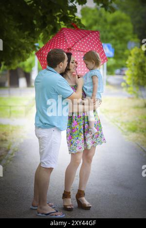 Giovane famiglia felice sotto ombrello sul marciapiede Foto Stock