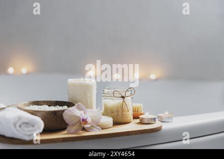 Preparazione per il trattamento termale dell'hotel, procedura per il bagno domestico. Lavabo bianco in bagno, accessori su vassoio candele brucianti, sapone, spazzola per piedi, asciugamano, Foto Stock