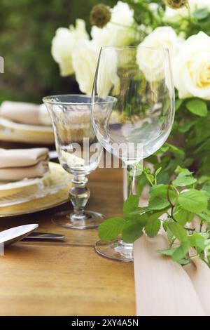 Candele e vaso con rose bianche collocate su tavola rotonda vicino agli occhiali da vino durante la romantica data in giardino Foto Stock