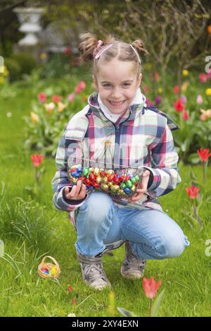 La bambina raccoglie le uova di pasqua in un cestino su un prato pieno di fiori in fiore in primavera Foto Stock