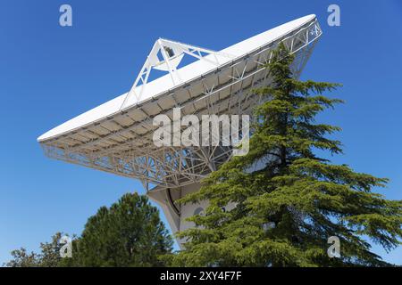 Radiotelescopio ESA sotto il cielo blu, parzialmente oscurato da alberi verdi, utilizzato per la ricerca scientifica, European Space Astronomy Centre, Villafranca del Foto Stock