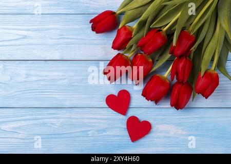 Tulipani rossi e due cuori di legno su blu sullo sfondo di legno, vista aerea con spazio di copia Foto Stock