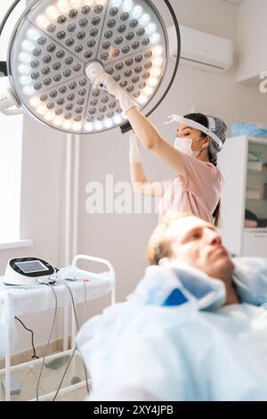 Shot focale selettivo verticale di infermiera in uniforme medica regolazione della preparazione della luce esecuzione di procedure mediche in clinica. Foto Stock