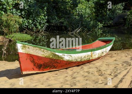 Vecchio di legno barca da pesca sulla sabbia della spiaggia accanto alla foresta tropicale Foto Stock