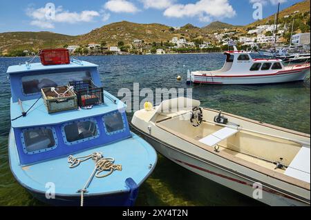 Tre diverse barche ancorate nelle acque cristalline in una giornata di sole di fronte a una pittoresca città portuale, Grikos Harbour, Grikos, Patmos, Dodecaneso, G Foto Stock