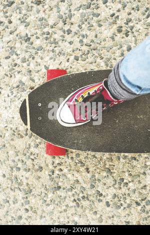 Dettaglio skateboard parzialmente grande con le gambe di una donna in sneakers Foto Stock