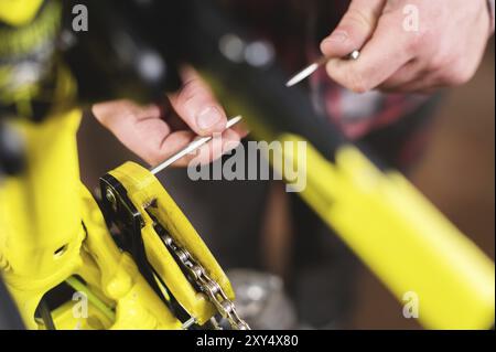 Manutenzione ravvicinata di una mountain bike. Le mani maschio regolano la tensione della catena. Monitoraggio delle condizioni tecniche in officina Foto Stock