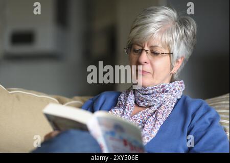Donna seduta su un divano e la lettura di un libro Foto Stock