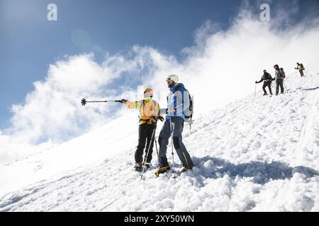 Gli scalatori professionisti completamente attrezzati scendono lungo le piste innevate con il sole. Uno degli scalatori punta con un bastone per tracciare da qualche parte Foto Stock