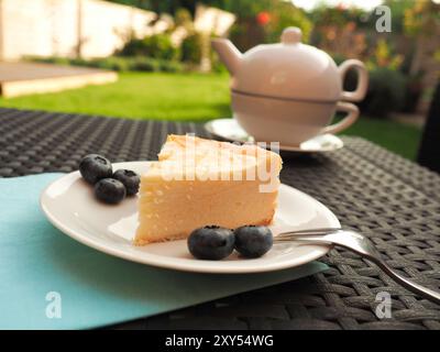 Pezzo di cheesecake con mirtilli su una piastra bianca su un tavolo da giardino Foto Stock