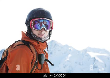 Ritratto di uno sciatore in una tuta arancione con uno zaino sulla schiena in un casco si staglia sullo sfondo di una splendida terra di montagna caucasica Foto Stock